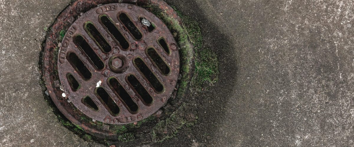 Close-up photo of a rusty drain grate with moss, offering a textured urban look.