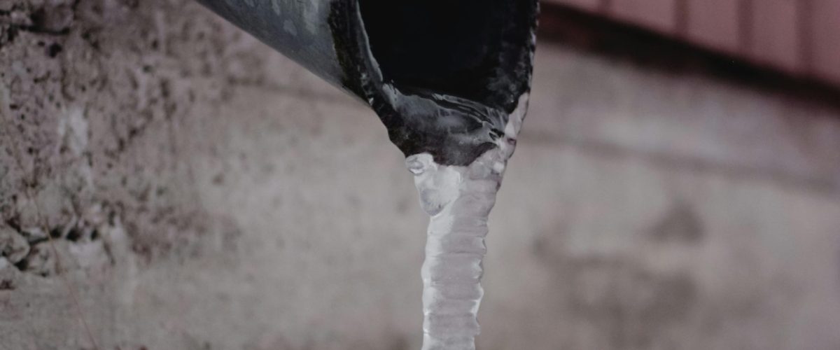 Frozen drain spout with icicle against a snowy backdrop. Captured in Estonia.