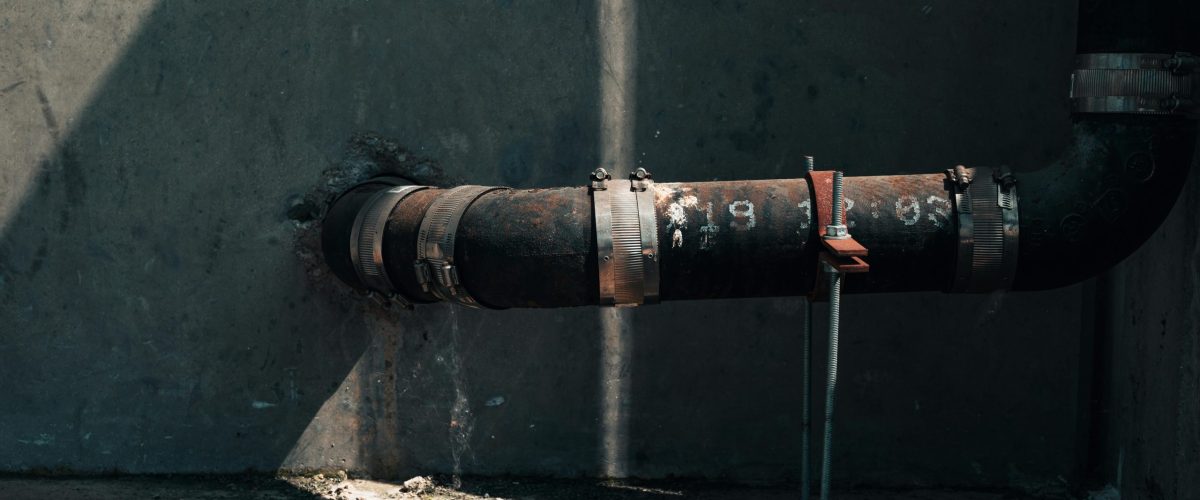 Rusted industrial pipe on a concrete wall with dramatic sunlight and shadows, showcasing urban decay.
